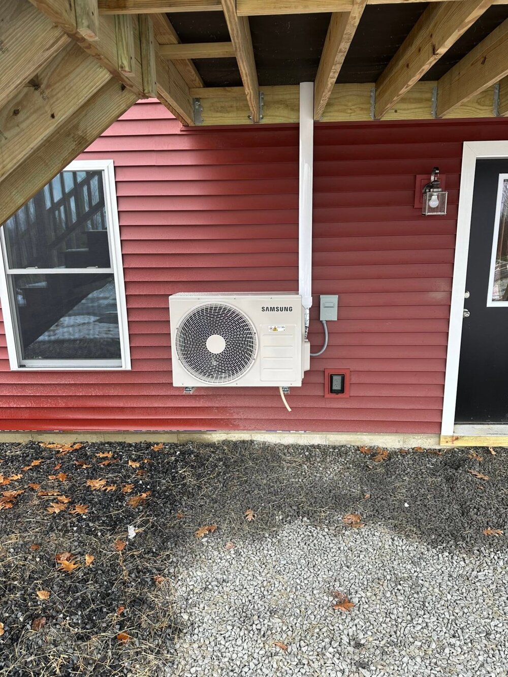 Samsung outdoor heat pump mounted on red siding — Barnett Heat Pumps